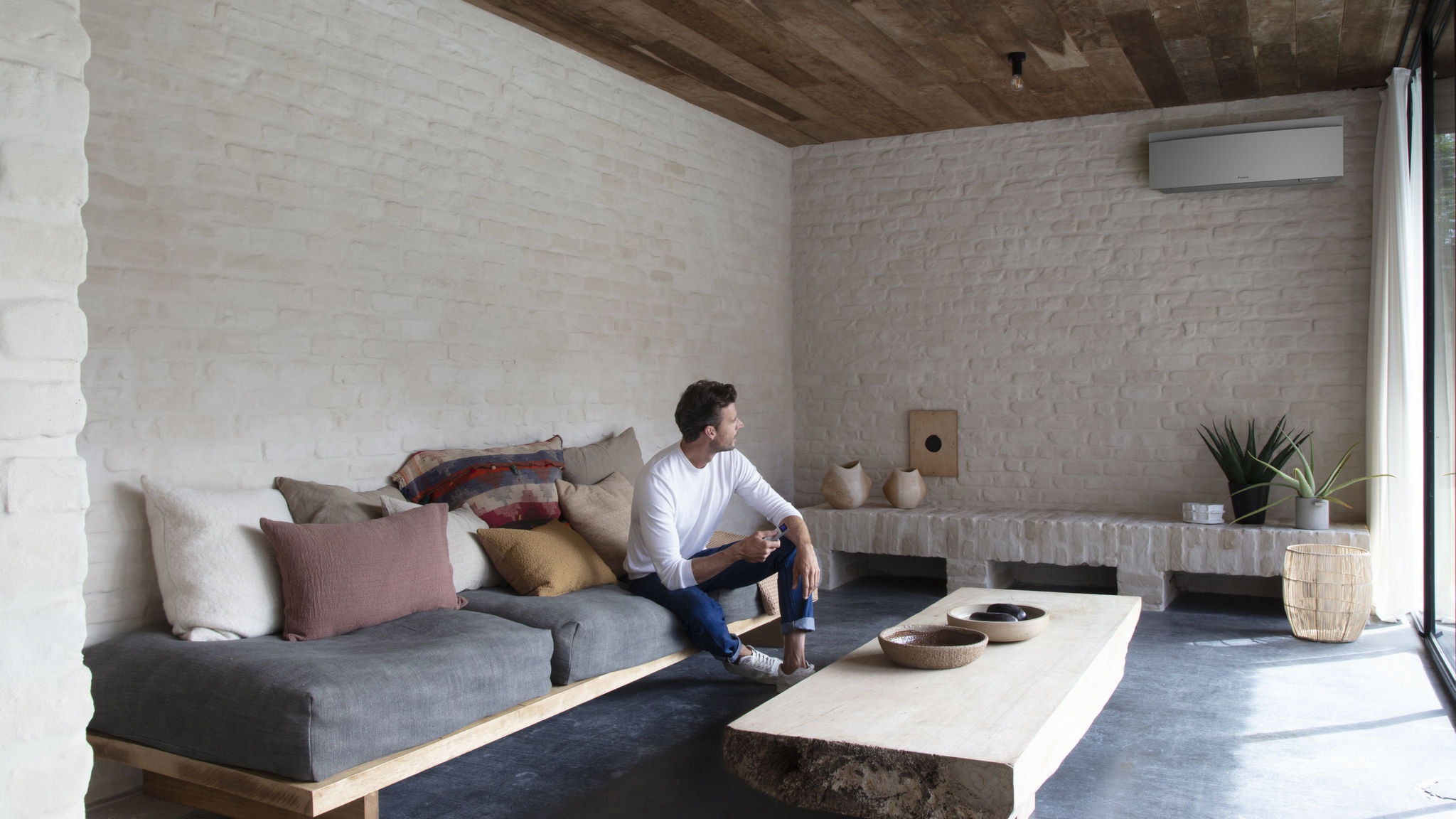 Mann auf einer Couch stellt an der Fernbedienung sein Comfora Innengerät auf die perfekte Temperatur ein